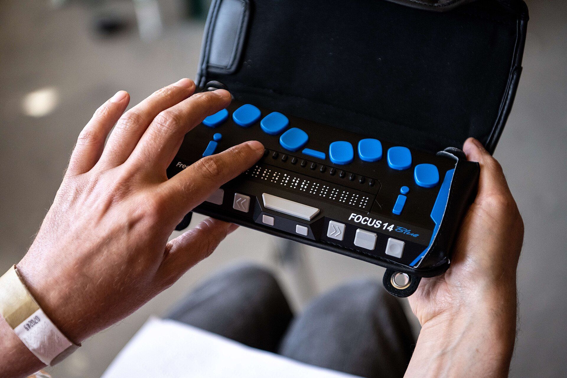 Las manos de una persona leen la línea braille de un dispositivo Focus 14 Blue que sostiene sobre el regazo