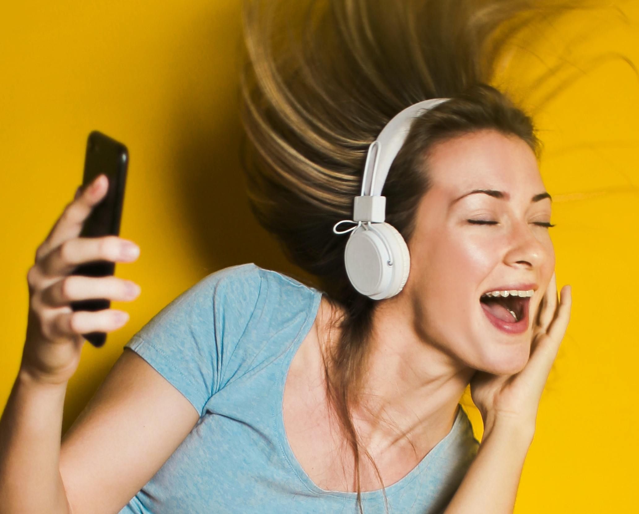 Una mujer joven canta con los ojos cerrados mientras escucha música con audífonos, con el teléfono en la mano
